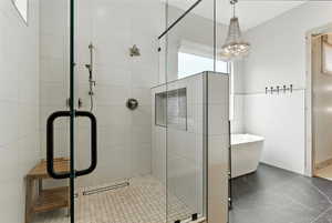 Full bath featuring a shower stall, tile walls, a freestanding tub, and a chandelier