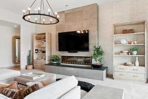 Living room featuring a tiled fireplace, built in shelves, a chandelier, and recessed lighting