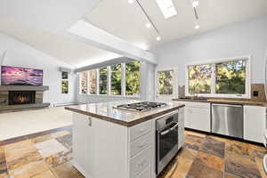 Kitchen with vaulted ceiling, skylights, open floor plan, white cabinetry, stainless steel appliances, and a center island