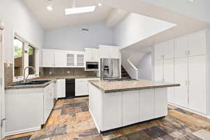Kitchen with vaulted ceiling, skylights, open floor plan, white cabinetry, stainless steel appliances, and a center island