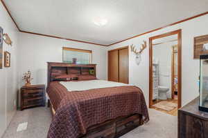 Bedroom with crown molding, a closet, a textured ceiling, ensuite bath, and light colored carpet