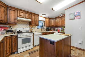 Kitchen featuring white appliances, a textured ceiling, light wood-type flooring, a center island, and backsplash