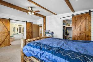 Bedroom with a barn door, ensuite bathroom, carpet floors, wood walls, and a textured ceiling