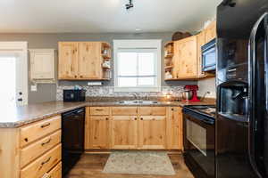Kitchen featuring black appliances, light brown cabinetry, open shelves, a peninsula, and dark wood-style flooring