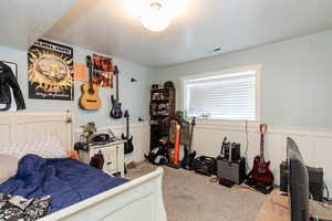Bedroom with a wainscoted wall, light colored carpet, a textured ceiling, and a decorative wall
