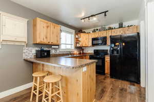 Kitchen with black appliances, a peninsula, open shelves, dark wood-type flooring, and a breakfast bar