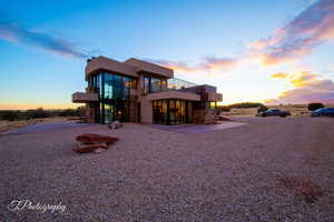 Back of house at dusk with stone siding, a balcony, and stucco siding