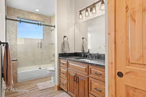 Full bath with enclosed tub / shower combo, vanity, and light wood-style flooring