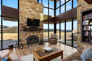 Living room featuring a towering ceiling, wood finished floors, an outdoor stone fireplace, and floor to ceiling windows