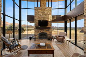 Living area with floor to ceiling windows, a stone fireplace, wood finished floors, a high ceiling, and healthy amount of natural light