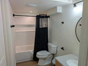Bathroom with a textured ceiling, shower / tub combo, vanity, and wood finished floors