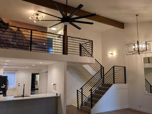 Stairs featuring beamed ceiling, high vaulted ceiling, wood finished floors, a chandelier, and a ceiling fan
