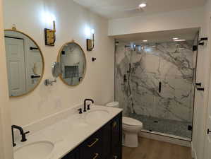 Full bathroom with a marble finish shower, double vanity, light wood-style floors, and recessed lighting