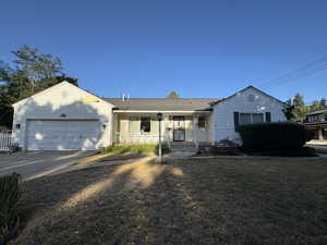 Ranch-style house with a garage, driveway, a front lawn, and a porch