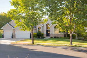 View of property hidden behind natural elements with stucco siding, driveway, a front yard, stone siding, and brick siding
