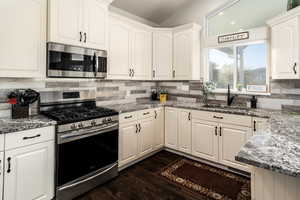 Kitchen with appliances with stainless steel finishes, dark stone counters, decorative backsplash, dark wood-type flooring, and lofted ceiling