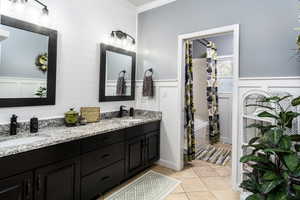 Bathroom featuring shower / tub combo with curtain, double vanity, light tile patterned flooring, a decorative wall, and ornamental molding