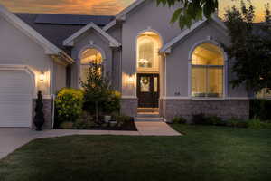 Doorway to property featuring a garage, stucco siding, a lawn, roof mounted solar panels, and brick siding