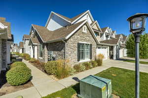 View of side of home featuring stone siding, board and batten siding, roof with shingles, concrete driveway, and a residential view