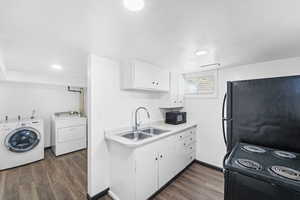 Kitchen with black appliances, light countertops, white cabinetry, dark wood-style flooring, and washer and clothes dryer