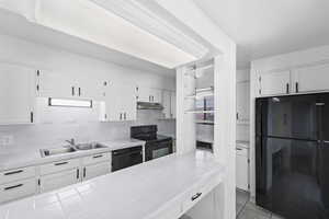 Kitchen with black appliances, white cabinets, backsplash, light tile patterned flooring, and tile counters