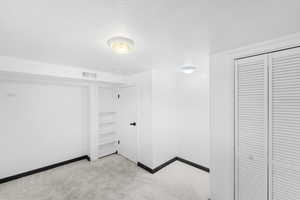 Unfurnished bedroom with light colored carpet, a textured ceiling, and a closet