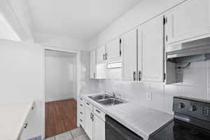 Kitchen with black appliances, decorative backsplash, white cabinets, tile countertops, and light tile patterned floors