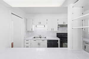 Kitchen featuring white cabinetry, tasteful backsplash, light countertops, and black appliances