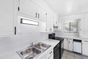 Kitchen with white cabinets, black appliances, decorative backsplash, and light tile patterned floors