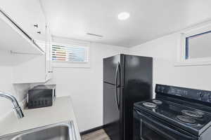 Kitchen featuring black appliances, white cabinets, light countertops, and light wood-style floors