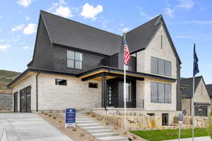 Rear view of property with stone siding, a porch, roof with shingles, and concrete driveway
