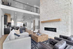 Living area featuring recessed lighting, light wood-type flooring, a stone fireplace, and a towering ceiling