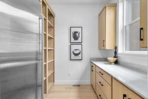 Kitchen with stainless steel fridge, light brown cabinetry, light wood-style floors, and light countertops