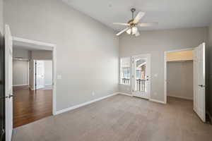 Unfurnished bedroom with light colored carpet, access to outside, high vaulted ceiling, a spacious closet, and ceiling fan