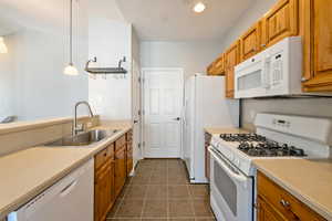 Kitchen featuring white appliances, decorative light fixtures, light countertops, brown cabinets, and dark tile patterned flooring