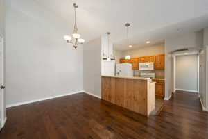 Kitchen featuring a peninsula, light countertops, hanging light fixtures, arched walkways, and dark wood-style floors