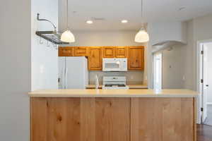 Kitchen featuring arched walkways, white appliances, hanging light fixtures, brown cabinetry, and recessed lighting