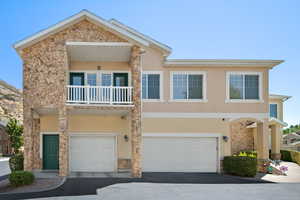 View of front facade featuring stone siding, a balcony, stucco siding, and a garage