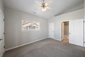 Unfurnished bedroom featuring vaulted ceiling, carpet floors, ceiling fan, and ensuite bath