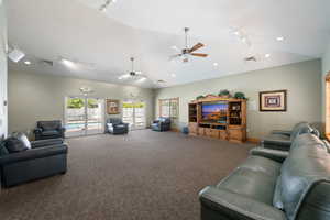 Living room featuring track lighting, vaulted ceiling, carpet flooring, a ceiling fan, and healthy amount of natural light