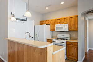 Kitchen with light countertops, white appliances, a peninsula, decorative light fixtures, and arched walkways
