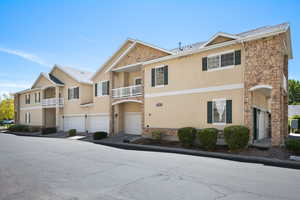 View of front facade featuring stucco siding, stone siding, a balcony, and an attached garage