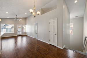 Spare room featuring recessed lighting, a chandelier, a towering ceiling, dark wood-style floors, and a ceiling fan