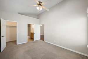 Unfurnished bedroom featuring a spacious closet, carpet, high vaulted ceiling, ensuite bathroom, and ceiling fan