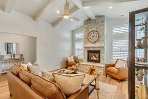 Living room featuring light wood-style flooring, ceiling fan, recessed lighting, a stone fireplace, and high vaulted ceiling