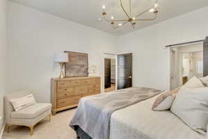 Bedroom with a walk in closet, a barn door, light colored carpet, and a chandelier