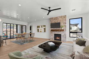 Living area with light wood-style floors, a stone fireplace, recessed lighting, and ceiling fan