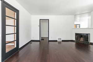 Unfurnished living room featuring dark wood-type flooring and a tile fireplace
