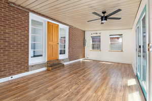 Unfurnished sunroom featuring brick wall, wood ceiling, wood finished floors, and ceiling fan