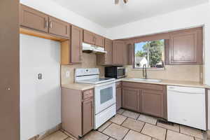 Kitchen with white appliances, light countertops, under cabinet range hood, decorative backsplash, and light tile patterned floors